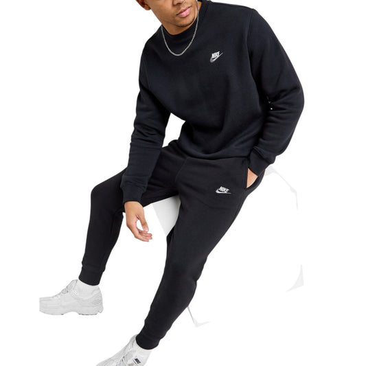 Person wearing a black Nike sweatshirt and pants with white sneakers on a white background