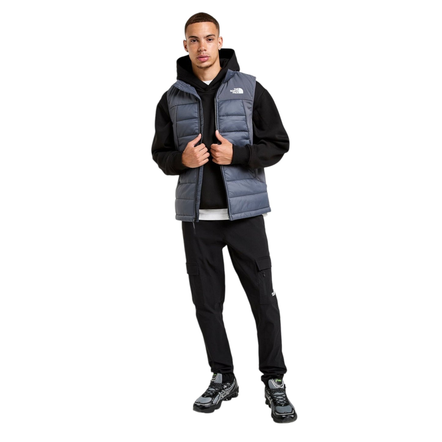 Person wearing a black hoodie, gray puffer vest, and black pants on a white background