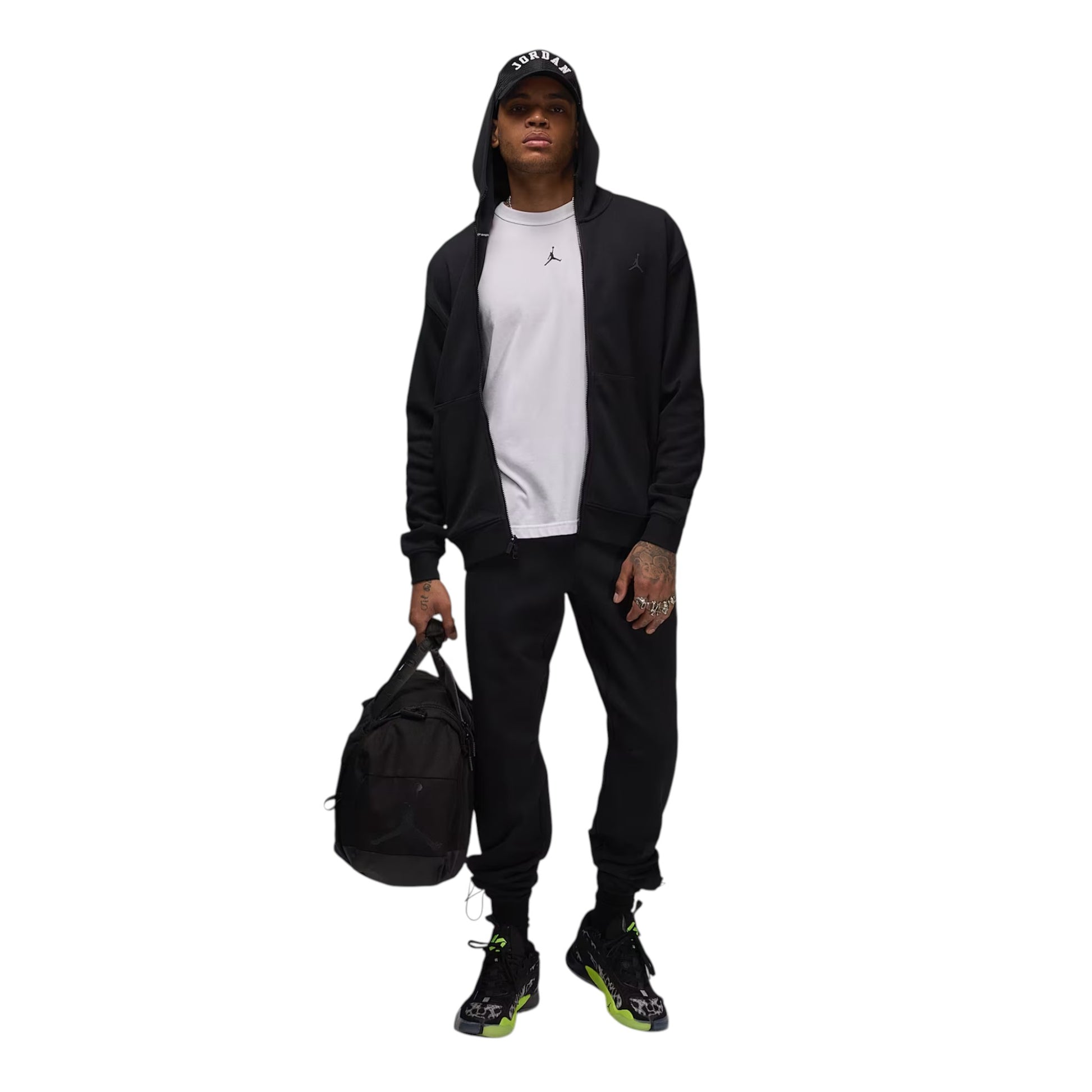 Person wearing a black tracksuit with a white shirt, holding a black bag on a white background