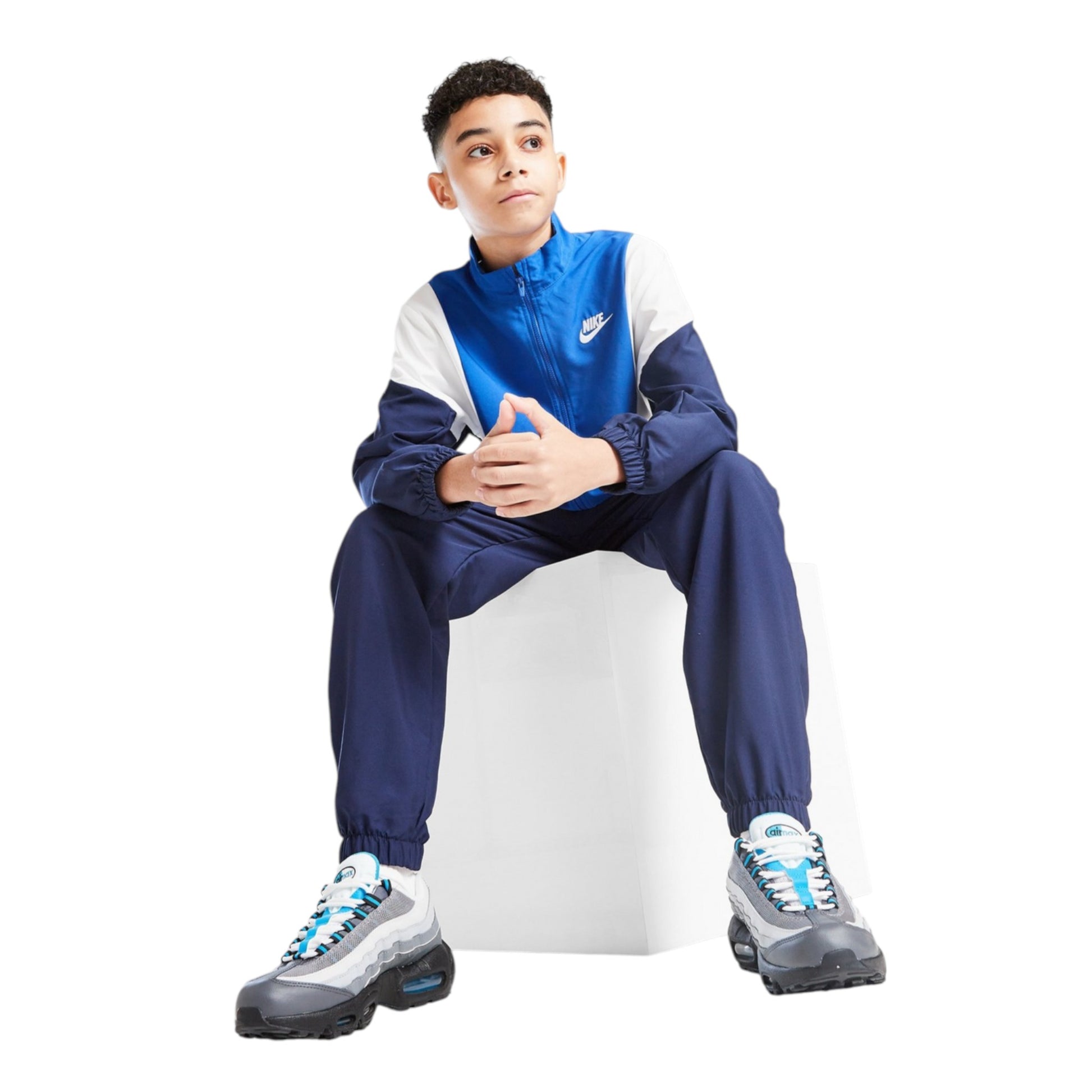 Person wearing a blue and white tracksuit with Nike logo, sitting on a white stool against a white background.