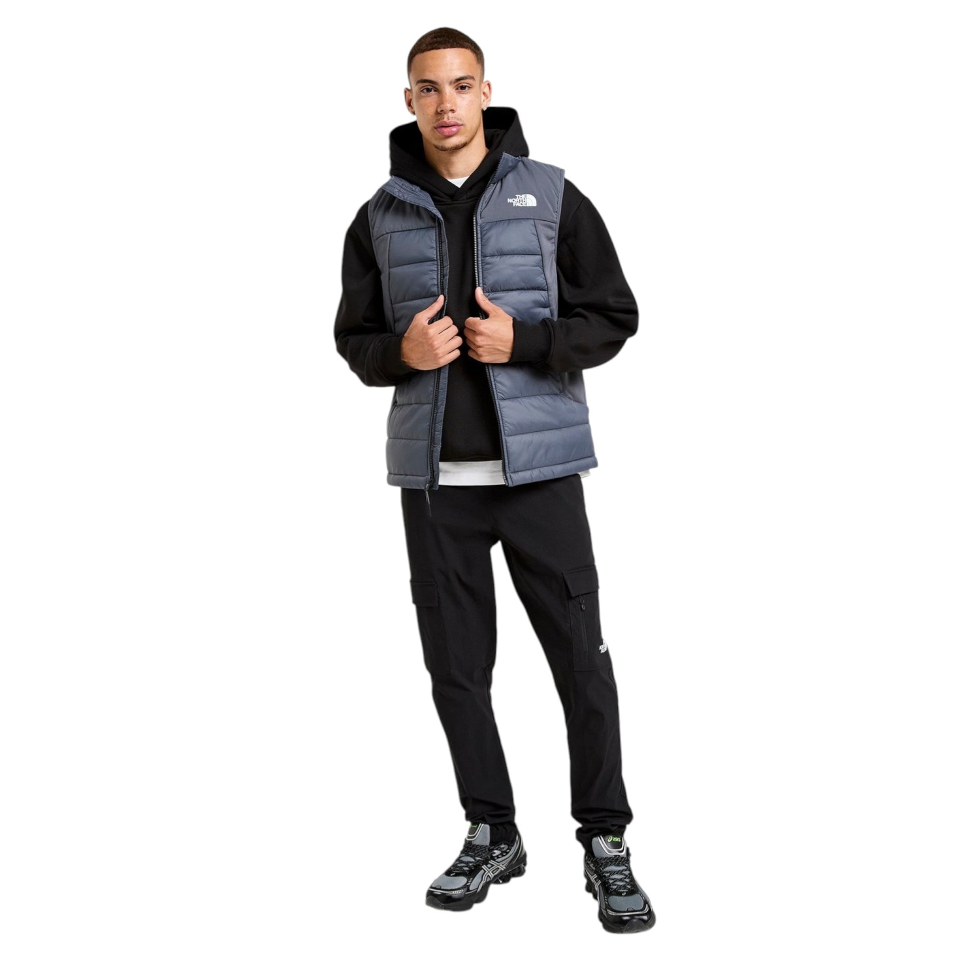 Person wearing a black hoodie, gray puffer vest, and black pants on a white background