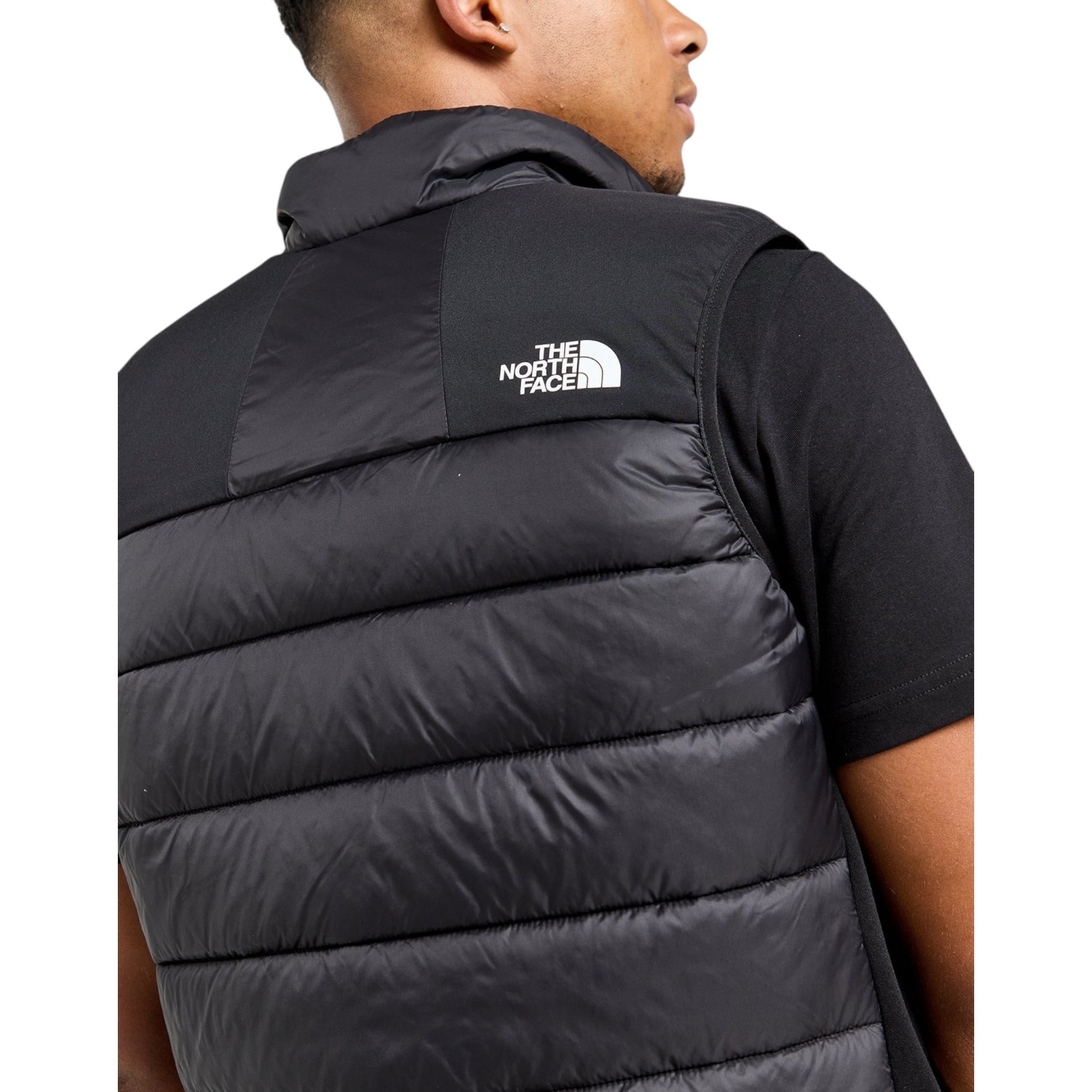Person wearing a black puffer vest with The North Face logo on a white background