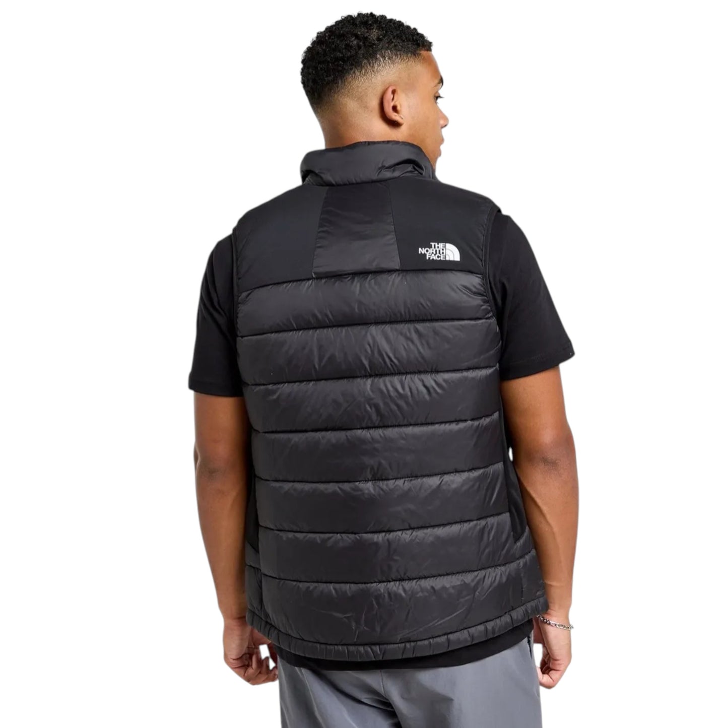 Person wearing a black puffer vest with The North Face logo on a white background