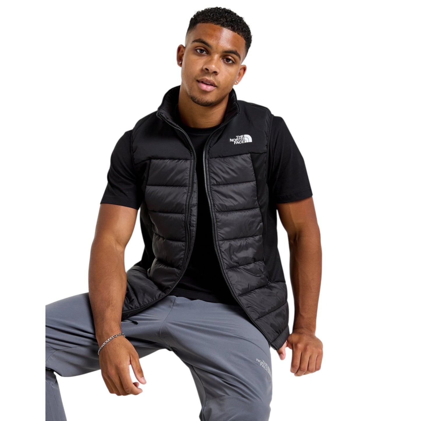 Man wearing a black puffer vest and gray pants on a white background